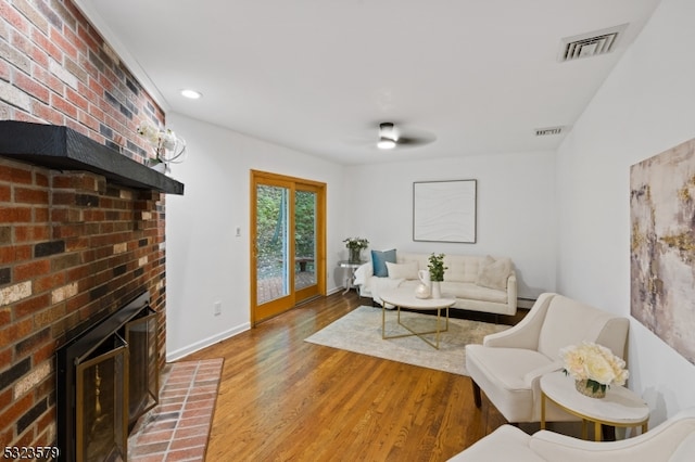 living room featuring a baseboard heating unit, hardwood / wood-style flooring, ceiling fan, and a brick fireplace