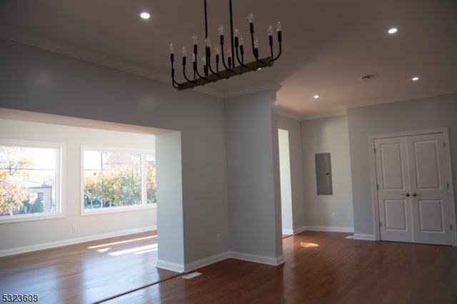 empty room featuring dark wood-type flooring, a chandelier, electric panel, and crown molding