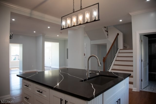 kitchen featuring dark hardwood / wood-style flooring, white cabinets, hanging light fixtures, an island with sink, and crown molding