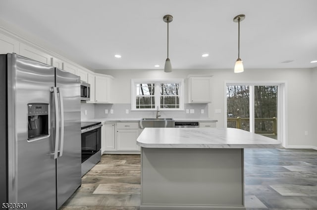 kitchen featuring pendant lighting, white cabinets, sink, a kitchen island, and stainless steel appliances