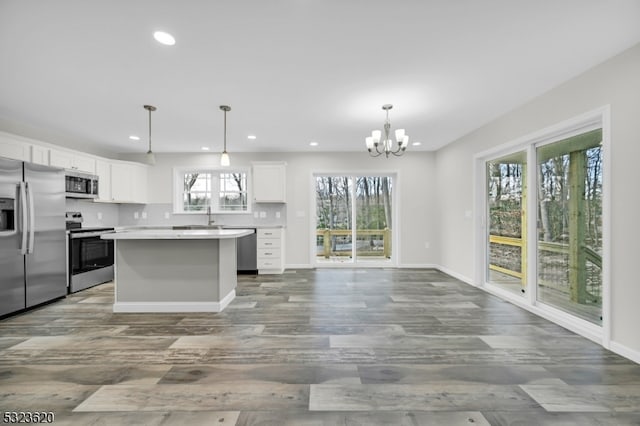 kitchen featuring appliances with stainless steel finishes, decorative light fixtures, a notable chandelier, white cabinets, and a center island