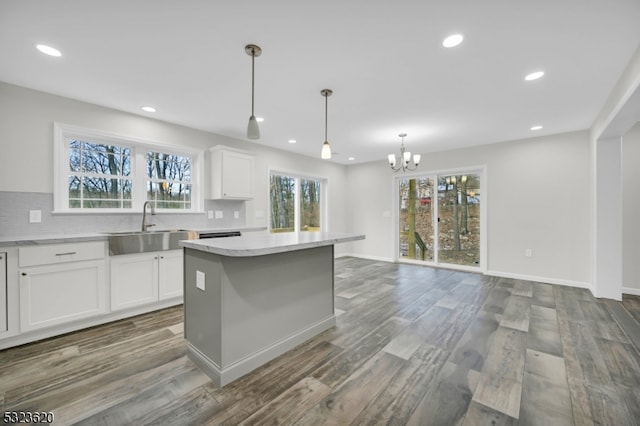 kitchen with sink, a kitchen island, dark hardwood / wood-style flooring, decorative light fixtures, and white cabinets