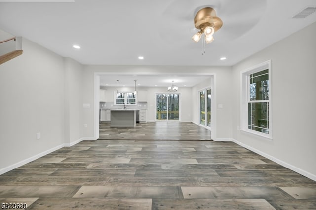 unfurnished living room featuring ceiling fan with notable chandelier, a healthy amount of sunlight, and dark wood-type flooring