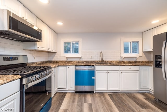 kitchen with dark stone counters, white cabinetry, appliances with stainless steel finishes, dark hardwood / wood-style floors, and sink