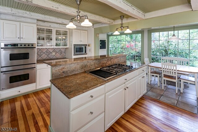 kitchen with appliances with stainless steel finishes, light hardwood / wood-style flooring, white cabinetry, and beam ceiling