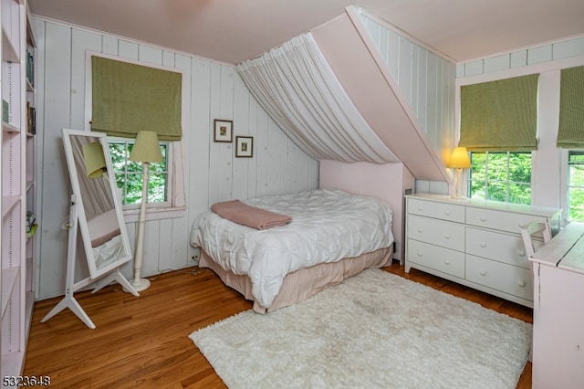 bedroom with wooden walls, lofted ceiling, and light wood-type flooring