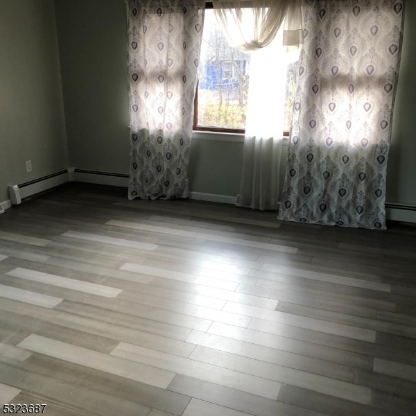 spare room featuring baseboard heating and light hardwood / wood-style flooring