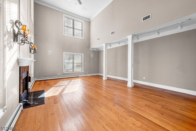 unfurnished living room with light hardwood / wood-style floors, a baseboard radiator, a healthy amount of sunlight, and ornamental molding