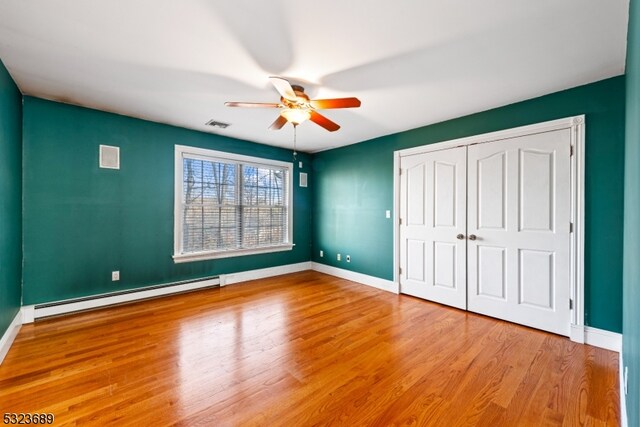 unfurnished bedroom featuring a closet, hardwood / wood-style floors, baseboard heating, and ceiling fan