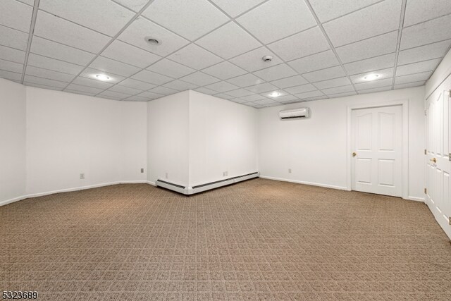 interior space with a drop ceiling, baseboard heating, an AC wall unit, and carpet