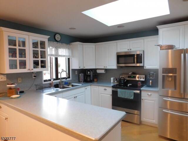 kitchen with a skylight, sink, stainless steel appliances, kitchen peninsula, and white cabinets