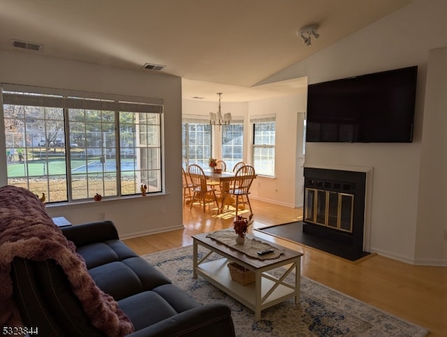 living room with light hardwood / wood-style floors, vaulted ceiling, and a notable chandelier