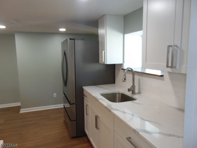 kitchen with dark wood-type flooring, white cabinets, sink, light stone countertops, and stainless steel fridge