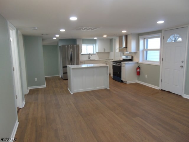 kitchen with dark hardwood / wood-style flooring, white cabinets, gas range, wall chimney range hood, and stainless steel fridge