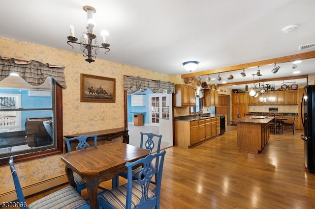 dining space with baseboard heating, sink, hardwood / wood-style floors, and an inviting chandelier