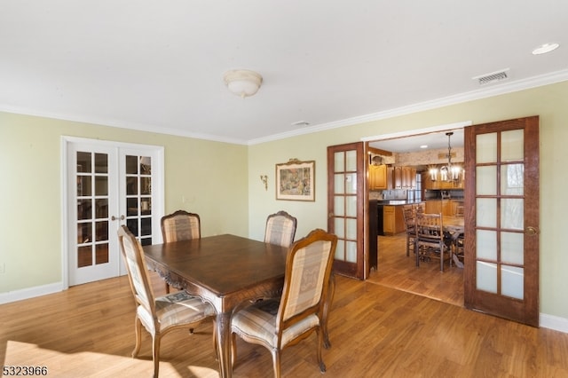 dining room with crown molding, french doors, an inviting chandelier, and light hardwood / wood-style flooring