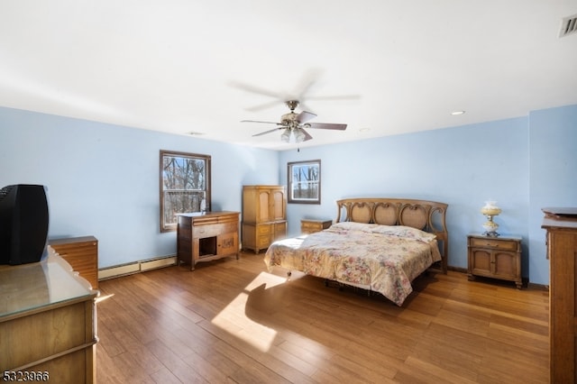 bedroom featuring hardwood / wood-style floors, baseboard heating, and ceiling fan