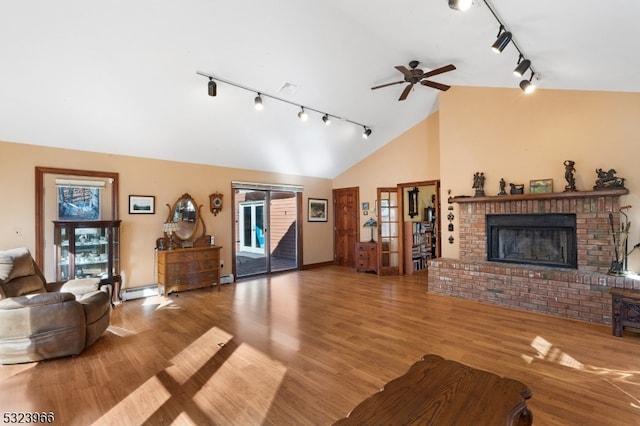 living room with high vaulted ceiling, track lighting, a brick fireplace, a baseboard radiator, and light hardwood / wood-style floors