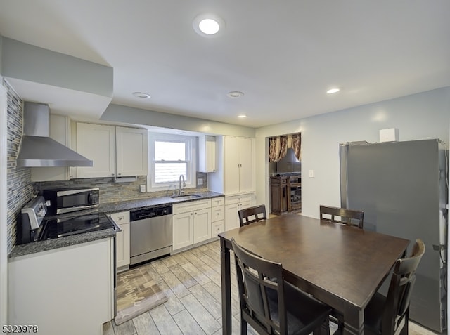 kitchen featuring wall chimney exhaust hood, white cabinetry, sink, and appliances with stainless steel finishes