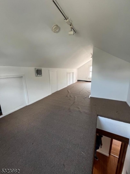 additional living space with dark colored carpet and vaulted ceiling