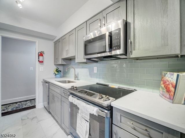 kitchen with gray cabinets, decorative backsplash, appliances with stainless steel finishes, and sink