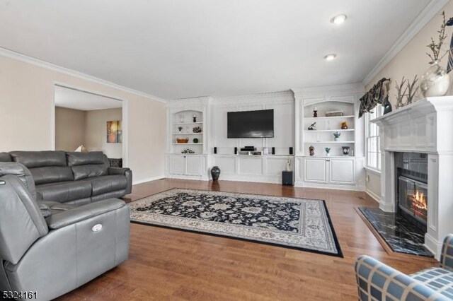 living area featuring wood finished floors, crown molding, built in shelves, and a fireplace