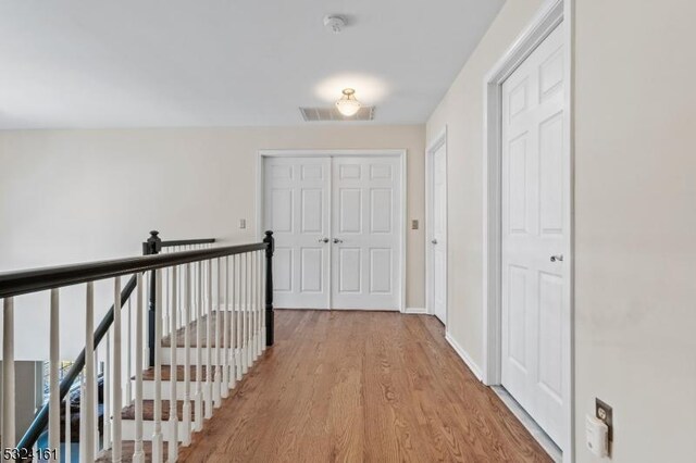 hall with visible vents, an upstairs landing, baseboards, and wood finished floors