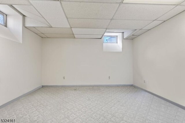 basement featuring a paneled ceiling, baseboards, and carpet flooring