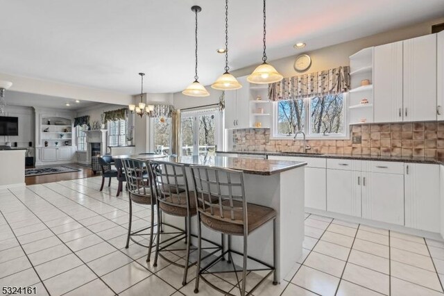 kitchen featuring open shelves, a sink, a kitchen island, a breakfast bar area, and light tile patterned floors