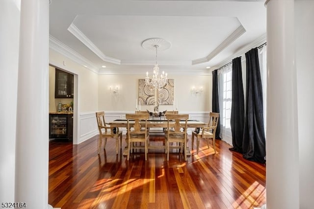 dining area featuring beverage cooler, hardwood / wood-style flooring, a tray ceiling, crown molding, and an inviting chandelier