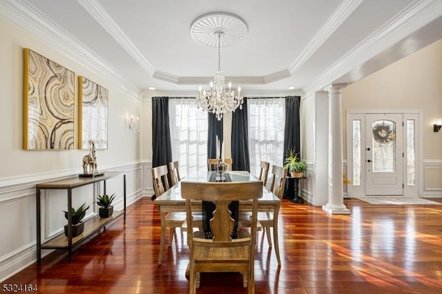 dining room with crown molding, dark wood-type flooring, a tray ceiling, a chandelier, and ornate columns