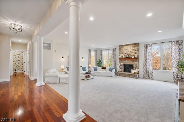 living room featuring a stone fireplace, wood-type flooring, a healthy amount of sunlight, and ornate columns