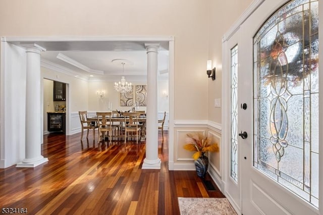 entrance foyer with dark wood-type flooring, crown molding, decorative columns, and a notable chandelier