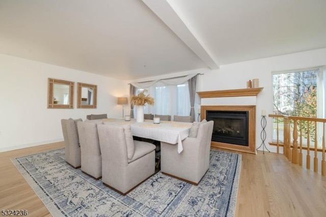 living area with a glass covered fireplace, beamed ceiling, wood finished floors, and baseboards