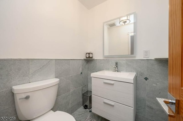 bathroom featuring tile walls, a wainscoted wall, toilet, and vanity