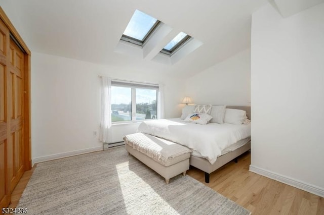 bedroom with vaulted ceiling with skylight, light wood-style flooring, baseboards, and baseboard heating