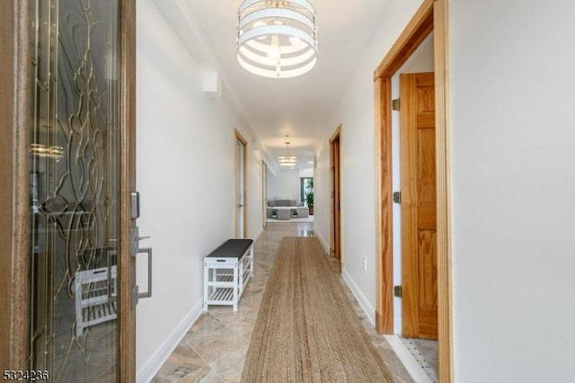 corridor featuring baseboards and a chandelier