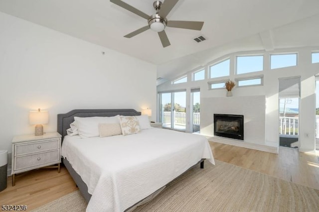 bedroom featuring light wood-type flooring, lofted ceiling, visible vents, and a tile fireplace