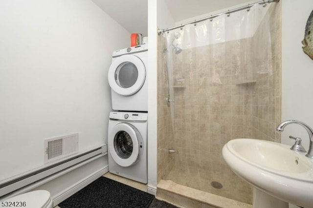 full bath with visible vents, stacked washing maching and dryer, a tile shower, a sink, and baseboard heating