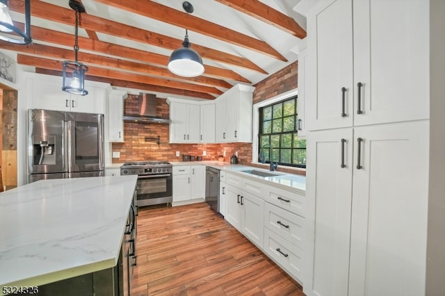 kitchen with stainless steel appliances, sink, hanging light fixtures, white cabinets, and wall chimney range hood