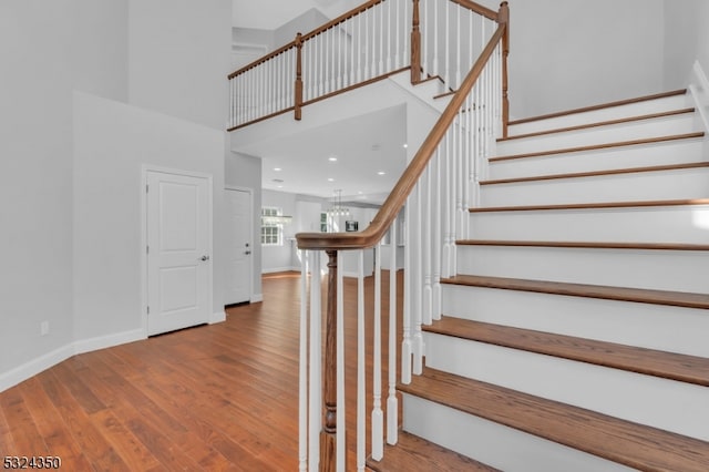 stairway featuring hardwood / wood-style floors, a towering ceiling, and a notable chandelier