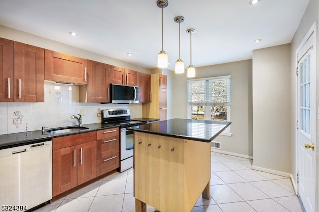 kitchen featuring sink, hanging light fixtures, decorative backsplash, appliances with stainless steel finishes, and a kitchen island