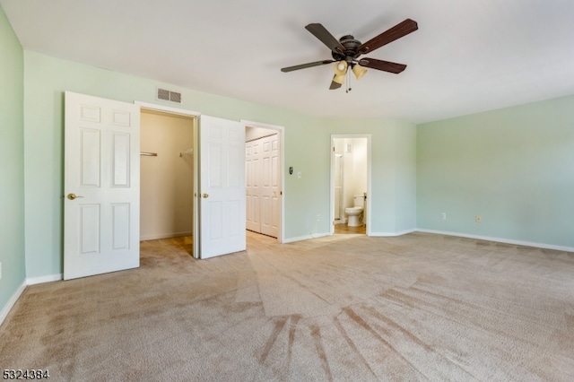 unfurnished bedroom featuring connected bathroom, a spacious closet, ceiling fan, and light carpet