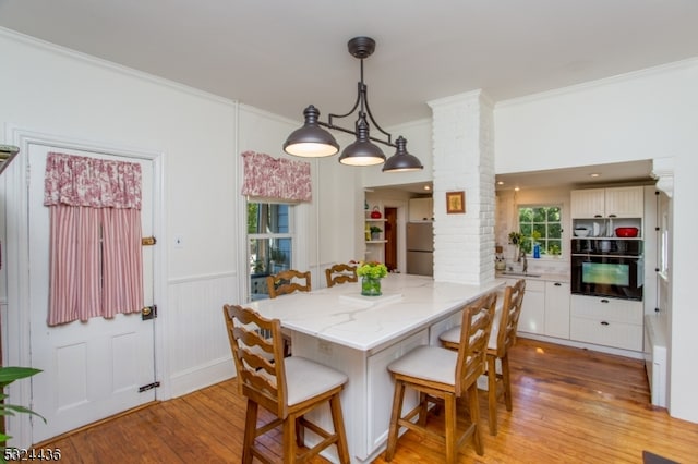 dining space featuring light wood-type flooring, decorative columns, crown molding, and sink