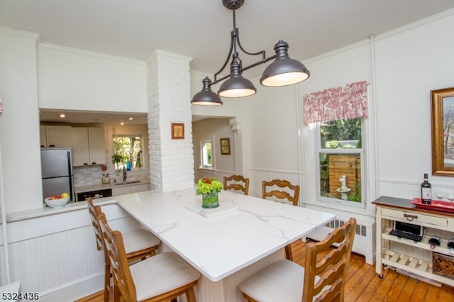 dining area with light wood-type flooring, ornate columns, radiator, crown molding, and sink