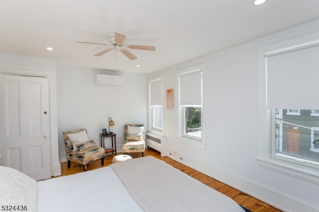 bedroom with hardwood / wood-style flooring, ceiling fan, radiator, and a wall mounted AC