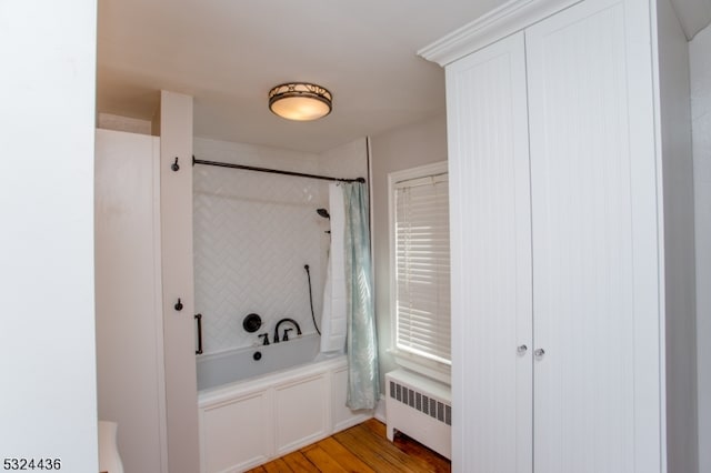 bathroom with hardwood / wood-style floors, shower / bathtub combination with curtain, and radiator