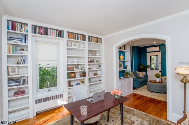 office space featuring crown molding, wood-type flooring, radiator heating unit, and an AC wall unit