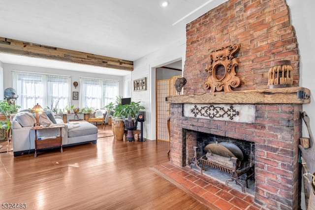 living room with beam ceiling, wood-type flooring, and a brick fireplace