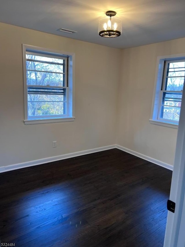 empty room featuring a healthy amount of sunlight, dark hardwood / wood-style floors, and an inviting chandelier